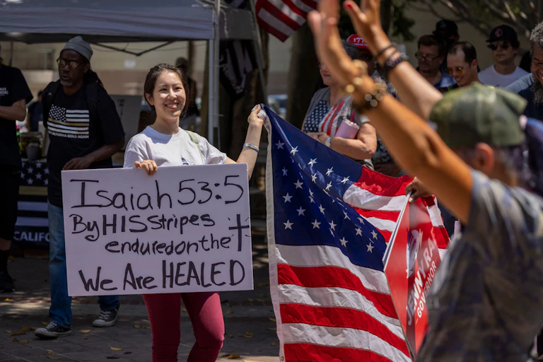 A woman holds a sign quoting Isaiah 53:5 in the Bible as anti-vaccination protesters pray and gather near City Hall in Los Angeles.