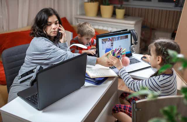 mother working on computer while looking after two young children