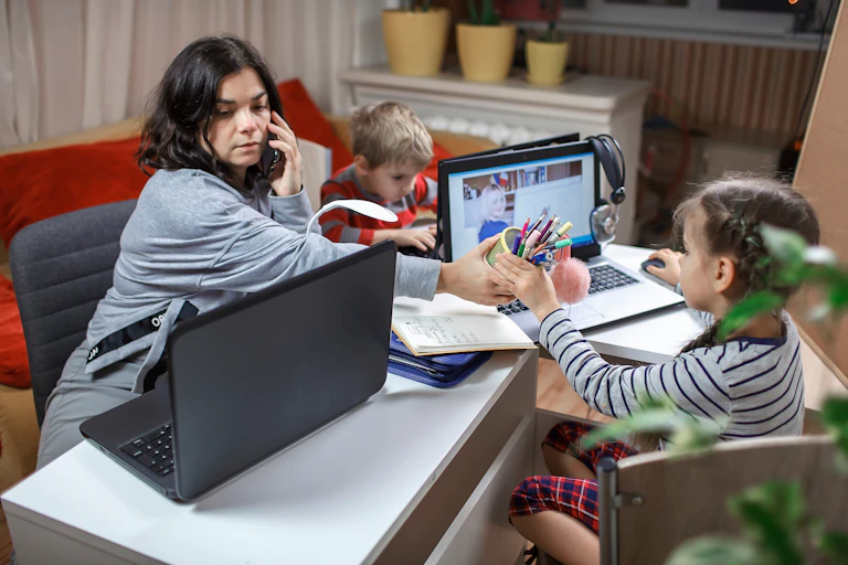 mother working on computer while looking after two young children