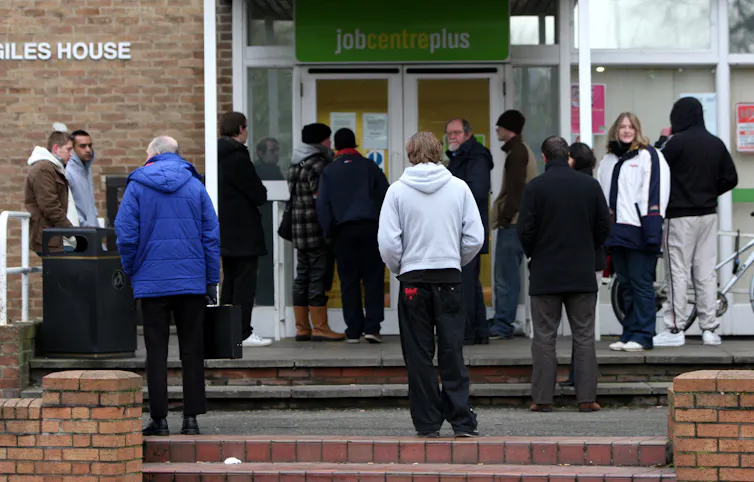 About a dozen people queuing outside of a Job Centre.