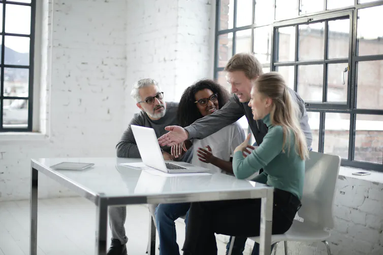 People sit at a table around a laptop talking