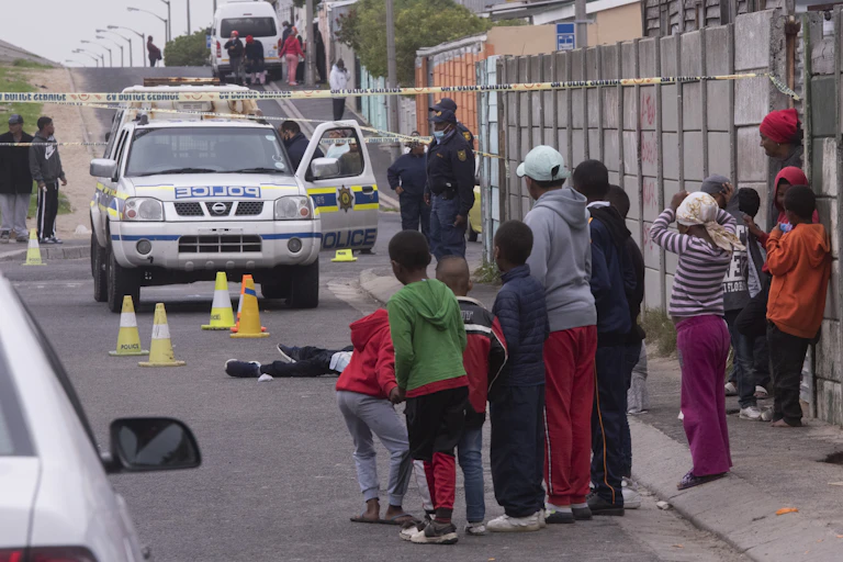Children watch as police investigate at a scene where a young man lies dead on the road