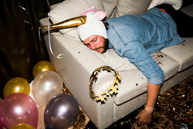 Homme ivre sur son canapé avec un chapeau de licorne.