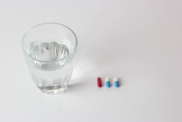 Un verre d’eau est placé à côté de deux cachets différents