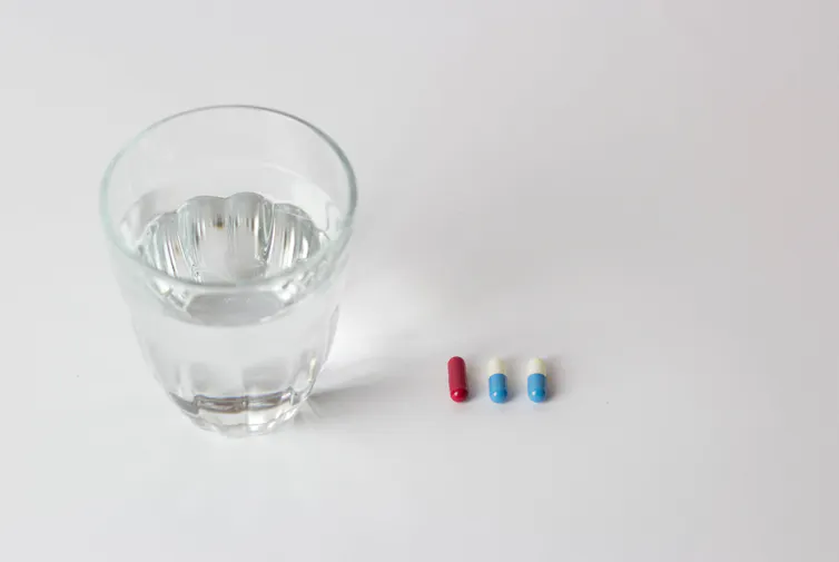 Un verre d’eau est placé à côté de deux cachets différents