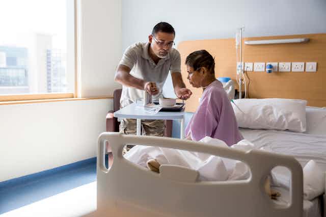 Person feeding an older patient sitting on a hospital bed.