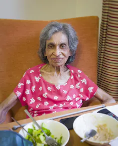 Indian older adult sitting in chair eating a meal.