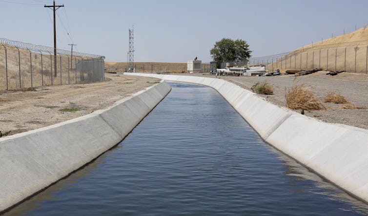 A concrete lined canal running through a dry landsacpe.