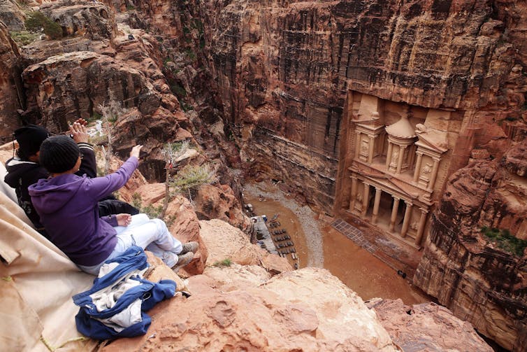 Tourists pointing to an ornate building facade carved out of red standstone.