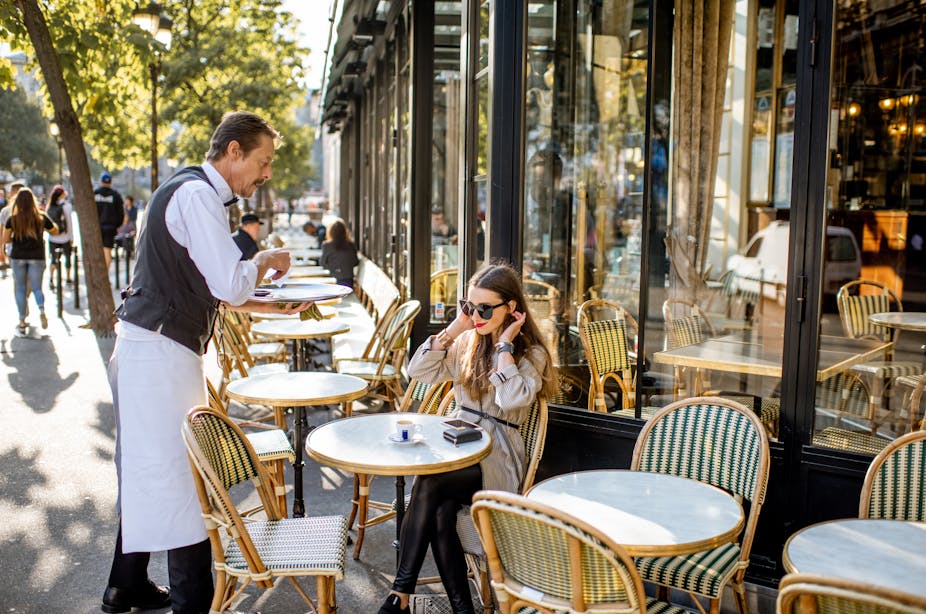 Waiter serving coffee to a young woman client sitting at the traditional french cafe outdoors in Paris.