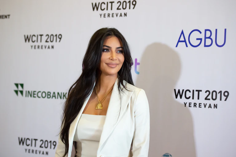 Kim Kardashian stands on a red carpet. Her hair is long and she's smiling off and to the left