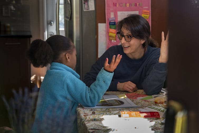 Woman and young girl sit at home table talking expressively