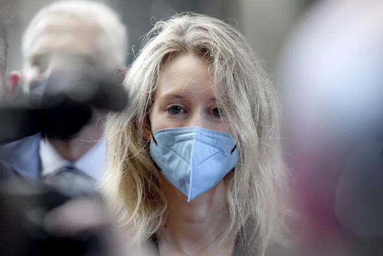Elizabeth Holmes arrives at court wearing face mask and staring straight into camera as a few other faces and heads are blurred