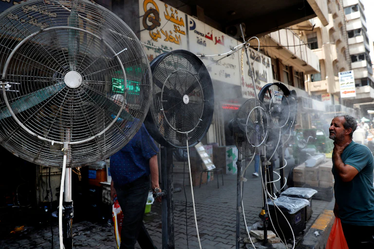A man stands in front of floor fans on a street in Baghdad