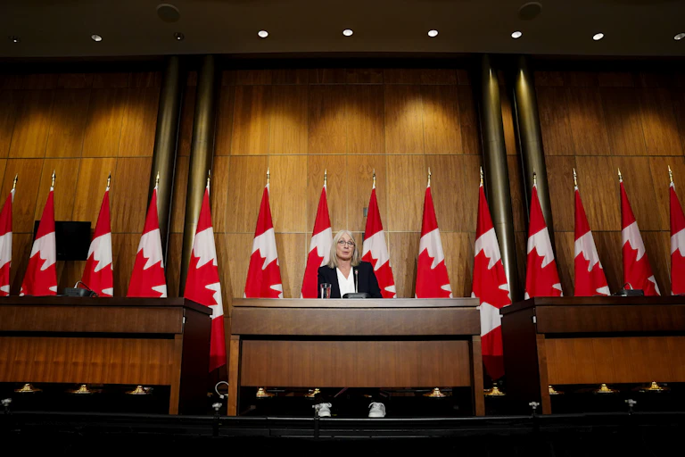Patty Hajdu stands at a podium in front of a row of Canadian flags