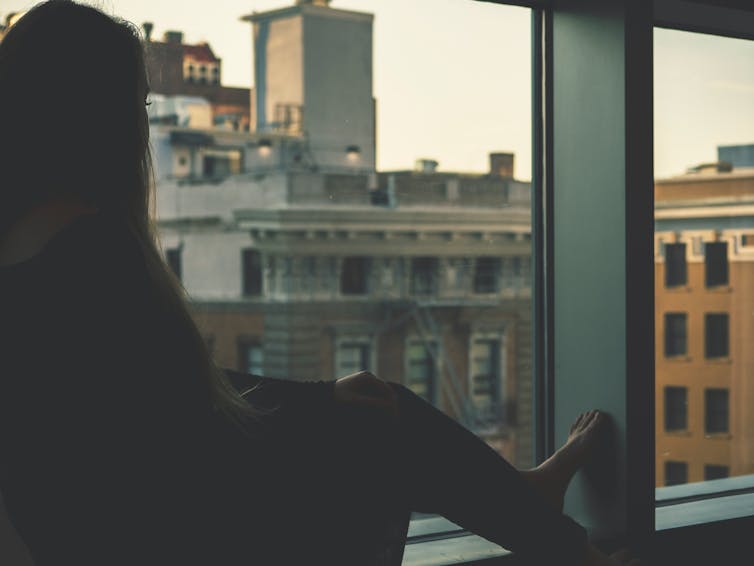 A woman looks out a window at a city street.
