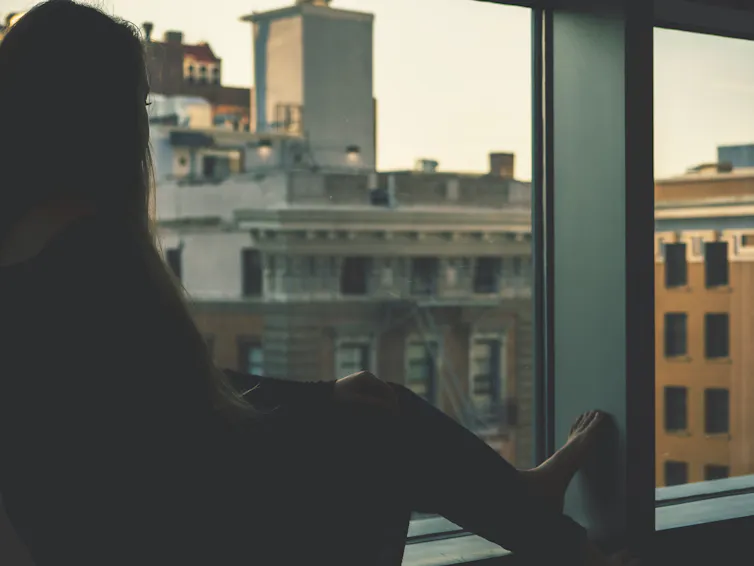 A woman looks out a window at a city street.