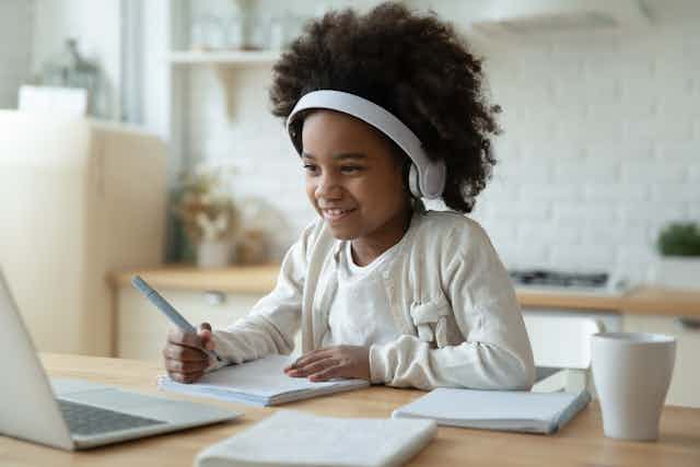 Girl at kitchen table learning on laptop with headphones on.