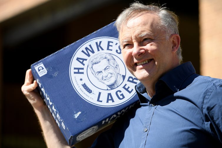 Anthony Albanese casually dressed carries a carton of Hawke's Lager on his shoulder.