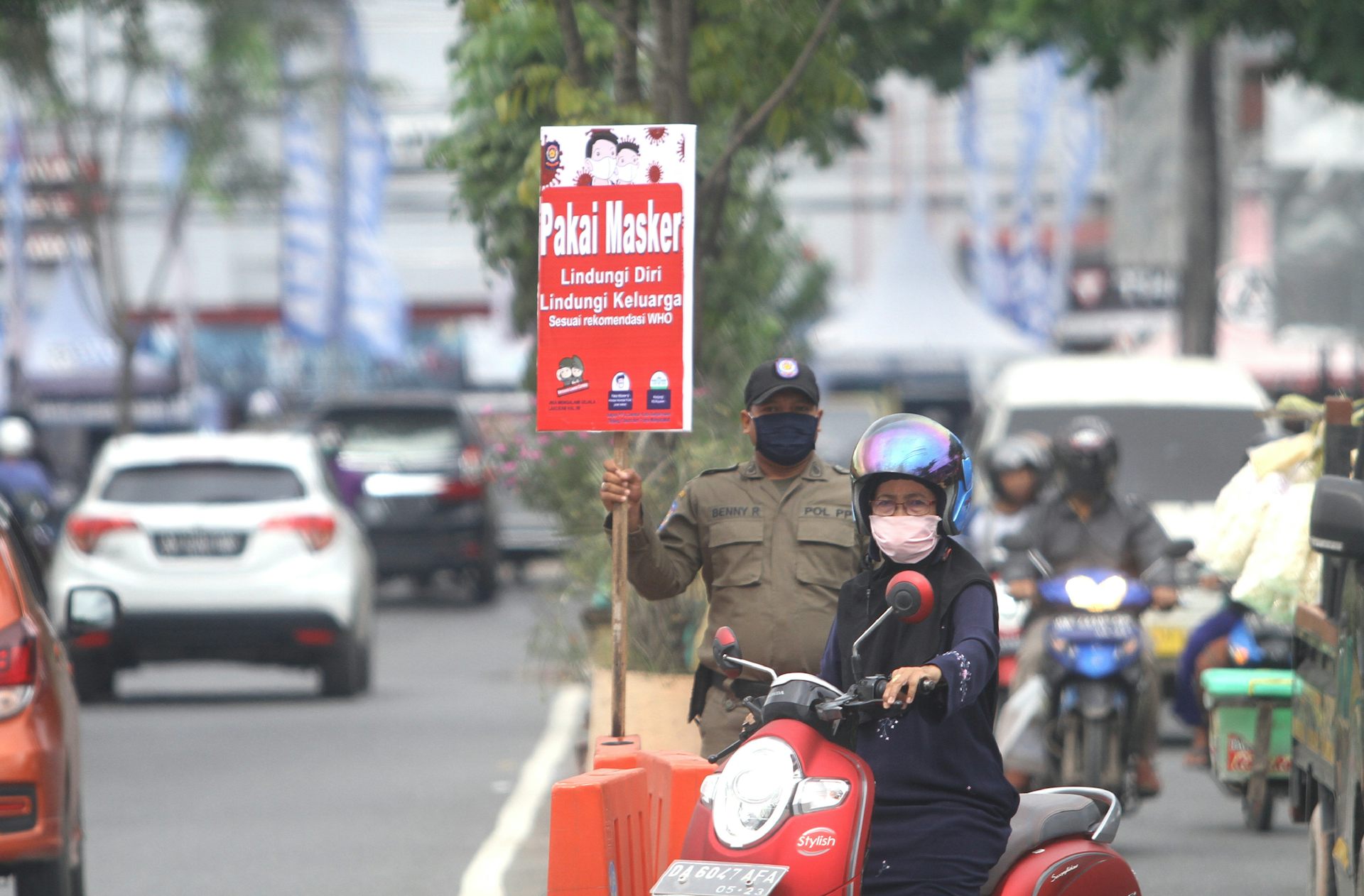 Petugas berdiri menunjukkan poster imbauan pencegahan COVID-19 di tepi jalan.