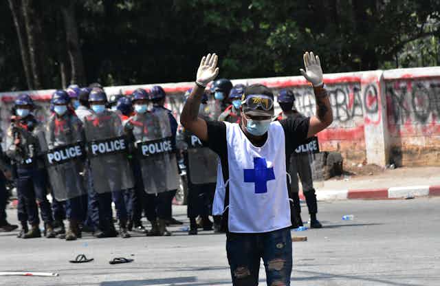 A medic walks away from a line of police with hands raised