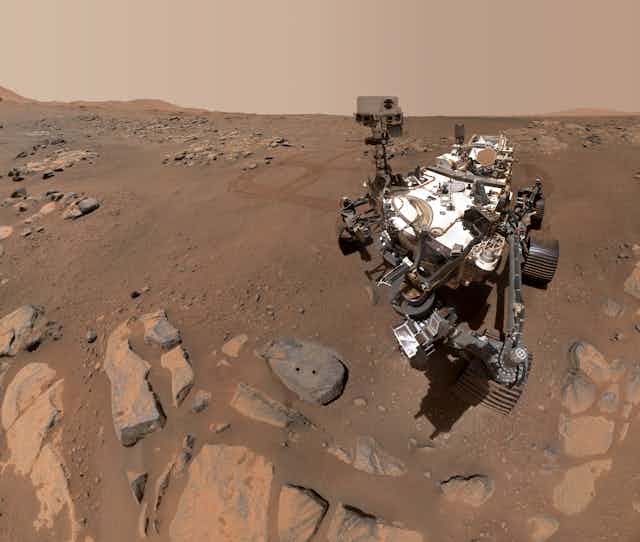A large Mars rover next to a rock with two circular holes.