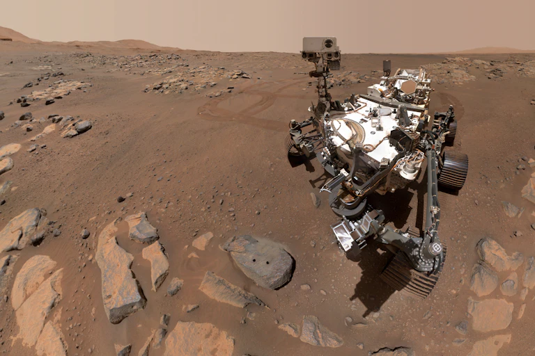 A large Mars rover next to a rock with two circular holes.