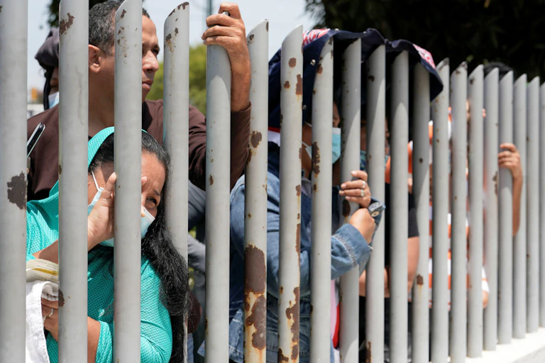 Men and women in COVID masks press their faces against the perimeter fence at Ecuador's Litoral Prison, September 2021.