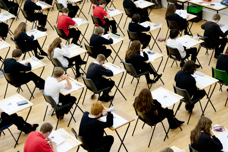 Rows of secondary-school students in uniform taking exams in a hall
