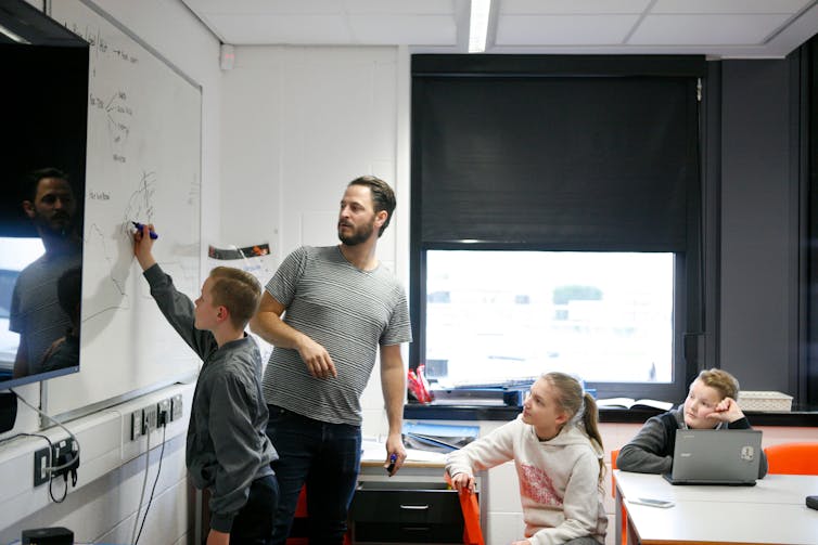 A teacher in a UK classroom with three students and lots of tech