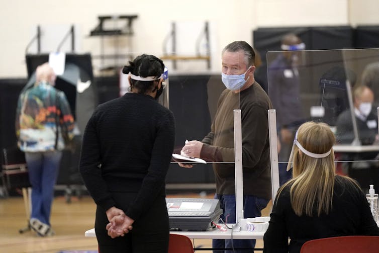 A voter and a poll workers, both wearing masks, have a conversation at a polling station.