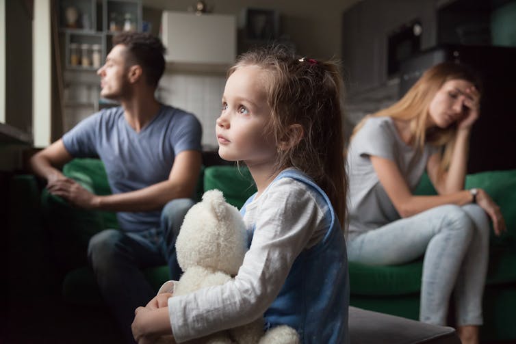 Child holding bear while parents look stressed out on couch.