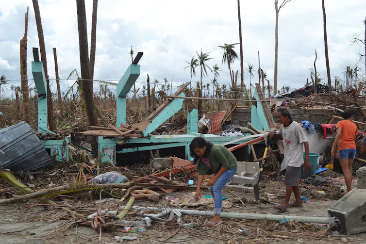 People in front of house destroyed by a typhoon.