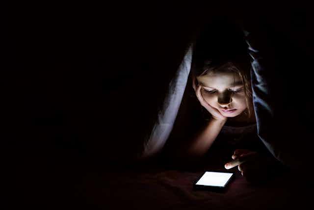 Girl under covers on phone at night.