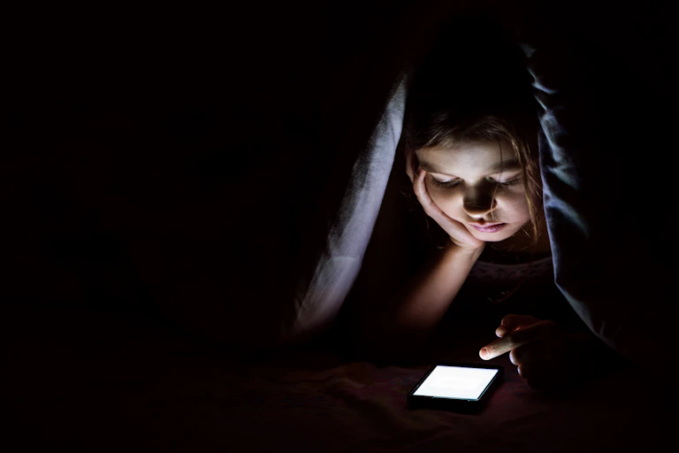 Girl under covers on phone at night.