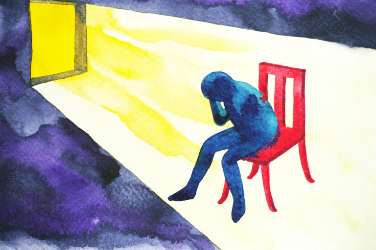 Illustration of blue human figure with its head in its hands, sitting in a red chair