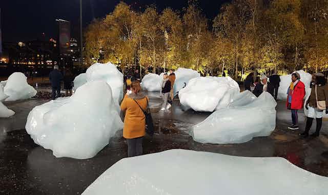 People stand around looking at giant melting blocks of ice.