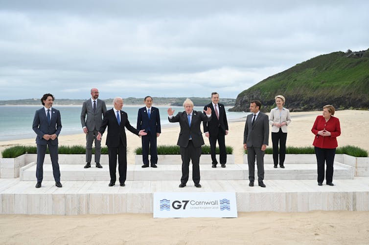 Boris Johnson está com os braços levantados na frente de outros líderes do G7 em uma praia.