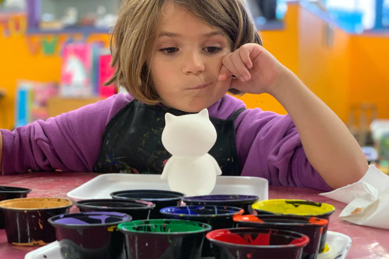 Young girl figuring out how to paint a cat figurine.