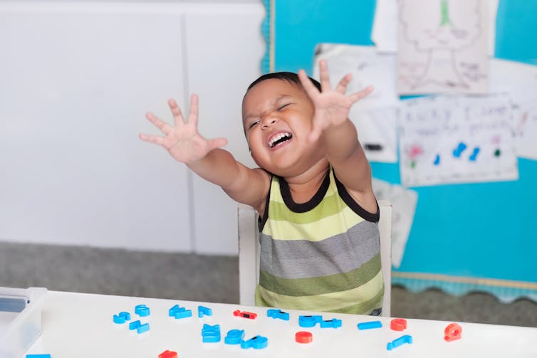 A boy in a classroom holding his hands out and yelling