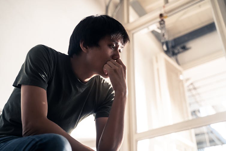 An Asian Australian man sits, looking contemplative.