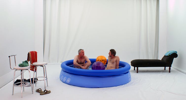 A stage. Two men in a wading pool.