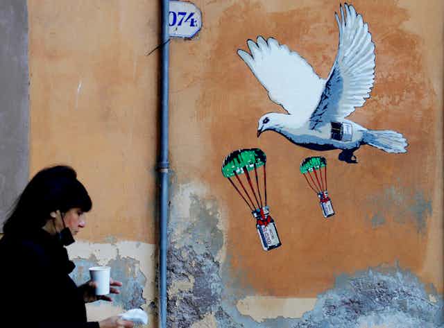A woman walks past a mural depicting a white dove parachuting COVID-19 vaccine vials