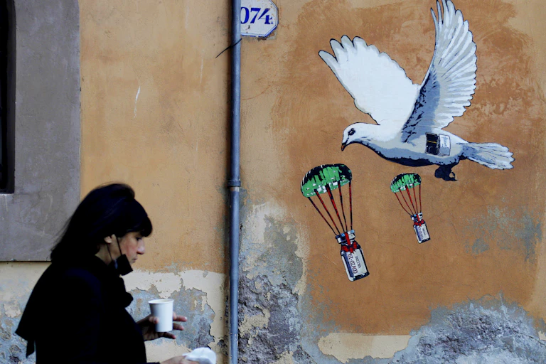 A woman walks past a mural depicting a white dove parachuting COVID-19 vaccine vials