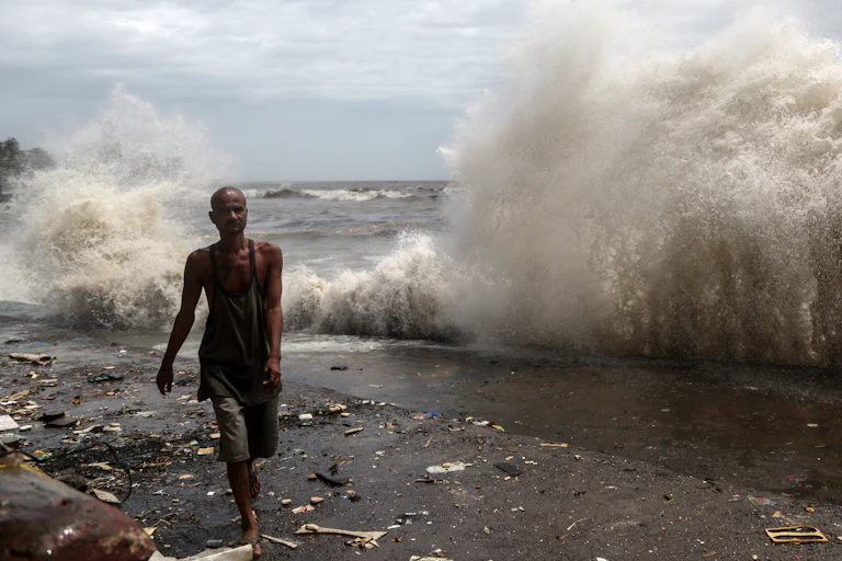 A man walks past a wave crashing on a seawall.