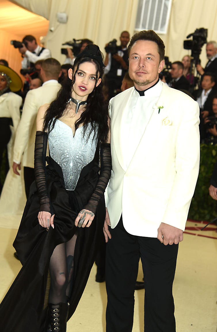 Grimes wears a gothic back and grey dress, Elon Musk wears a white dinner jacket.