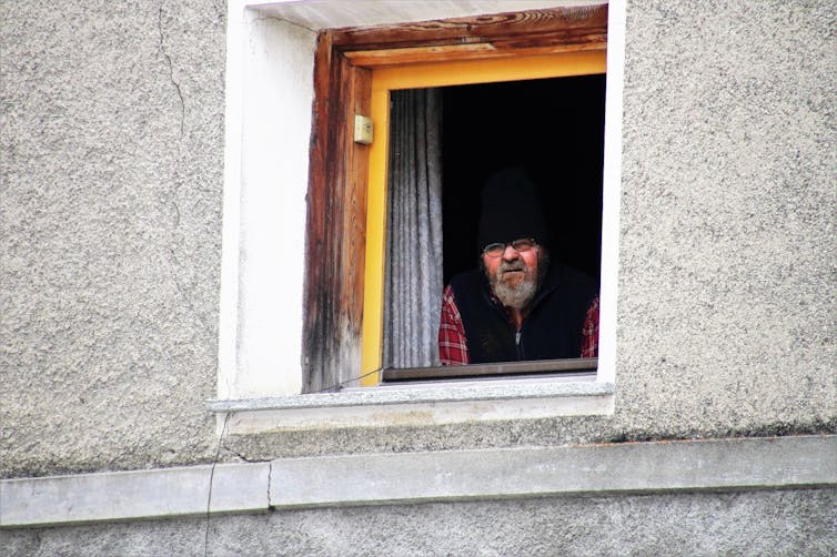 A warmly dressed person looks out of a window