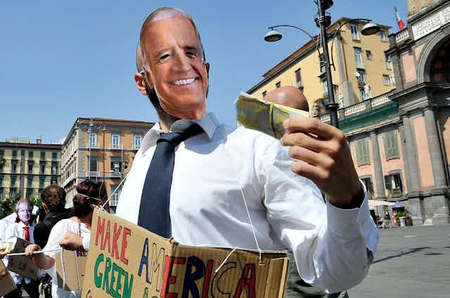 A protester wearing a Joe Biden mask brandishes a wad of cash.