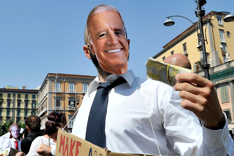 A protester wearing a Joe Biden mask brandishes a wad of cash.
