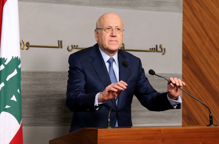 Najib Mikati, places one hand over a microphone at a press conference.